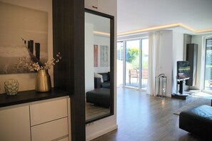 Un salon moderne avec un grand miroir, un canapé noir, une table en verre et un téléviseur.