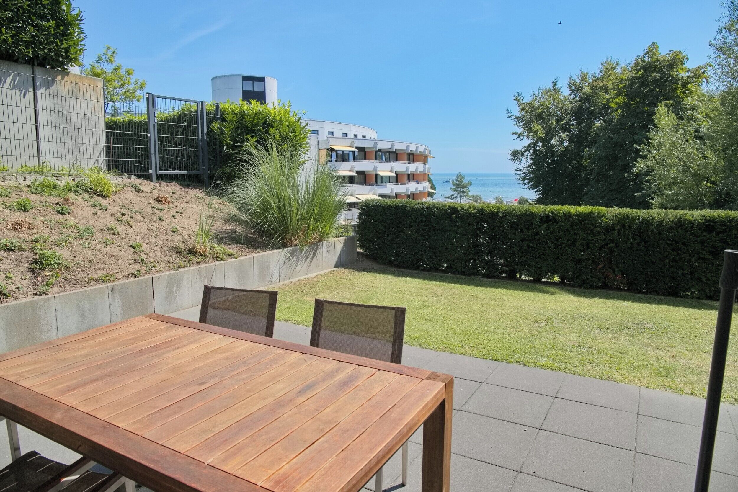 Un patio con mesa y sillas de madera, vista al mar y un edificio con balcones.