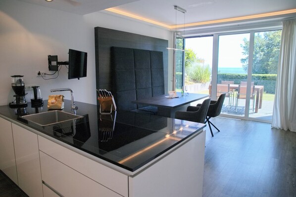 A modern kitchen with a large island, a flat-screen TV, and a dining area with a view. - Sealounge Whg. 1 Inkl. Wlan (Grömitz)