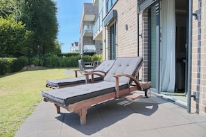 Two lounge chairs with cushions outside a building with a brick facade and a glass door.