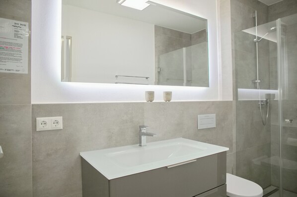 A modern bathroom with a large mirror, a white sink, and a glass-enclosed shower. - Sealounge Whg. 1 Inkl. Wlan (Grömitz)