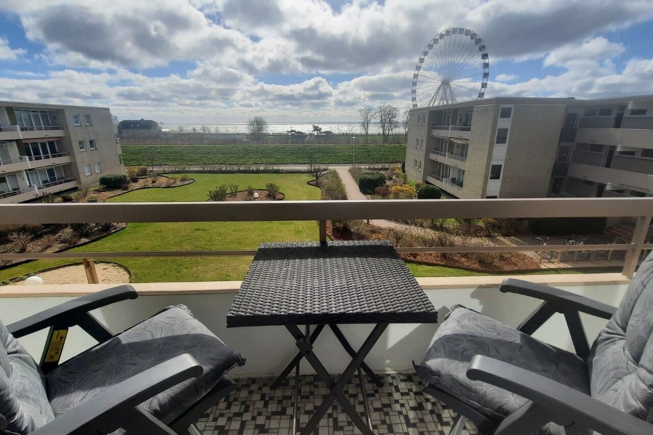 Un balcon avec vue sur une grande roue, une pelouse et des bâtiments modernes.