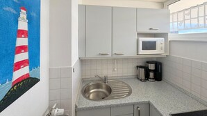 A kitchen with a stainless steel sink, white cabinets, a microwave, and a coffee maker. - Haus Baltic App. 188 Inkl. Wlan (Grömitz)