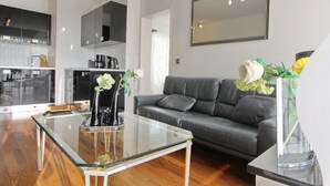 Un soggiorno moderno con un tavolino in vetro, un divano grigio e una zona cucina sullo sfondo.