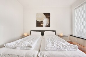 A double bed with white bedding, a bedside table with a lamp, and a wall-mounted artwork.