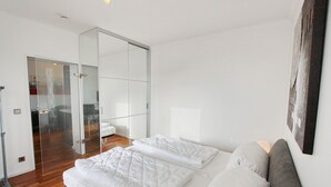 Una camera da letto moderna con un letto grande, una porta in vetro che dà su un bagno e un pavimento in legno.