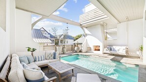 Ein Poolbereich mit Holzterrasse, einer Couch mit Kissen und einer hängenden Leuchte.