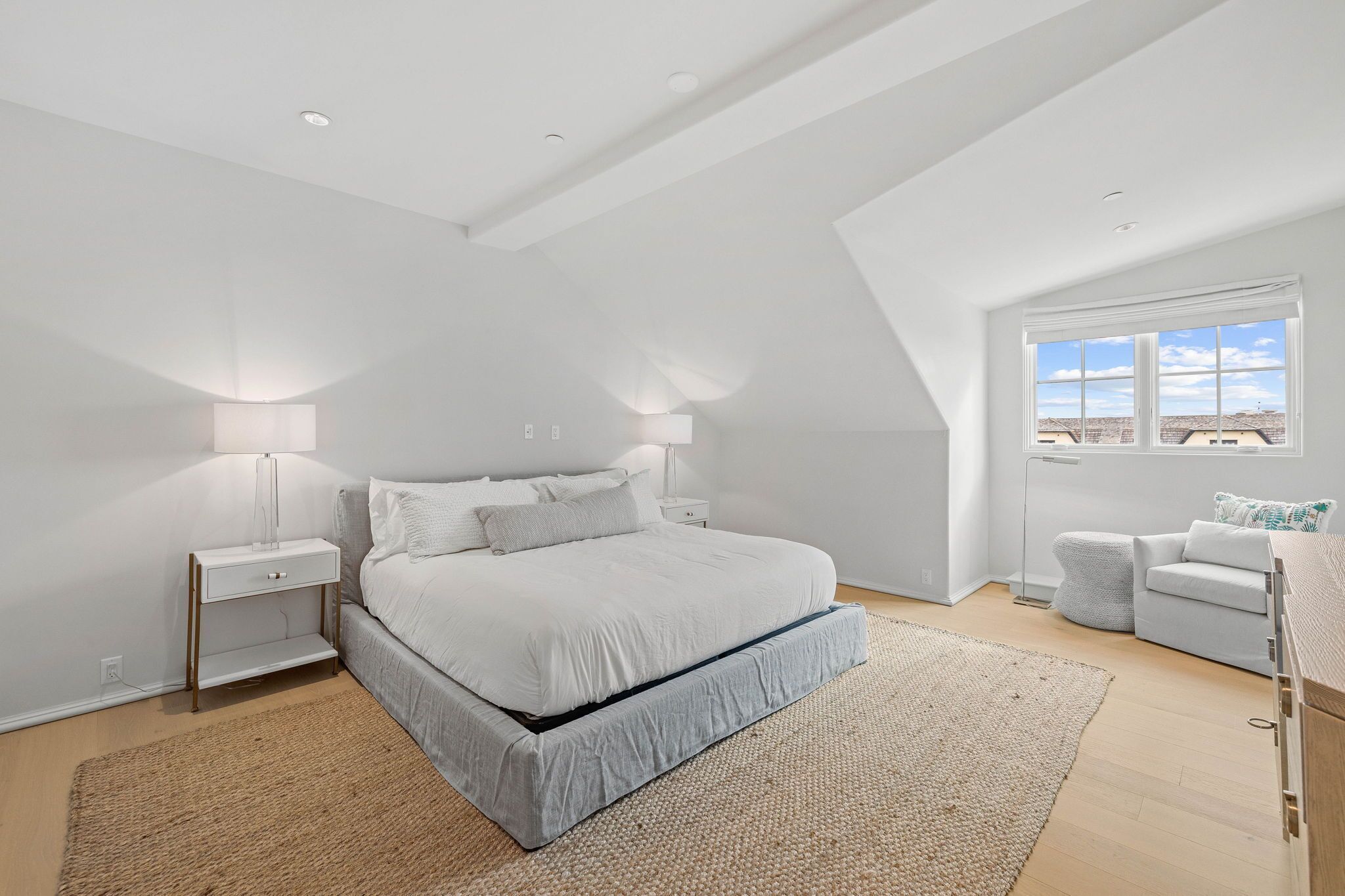 A bedroom with a bed, bedside lamps, a nightstand, a sofa, and a window with a view.