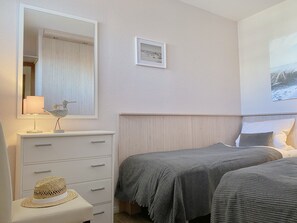 Une chambre avec deux lits, une commode, un miroir et un tableau encadré au mur.