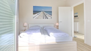 A bedroom with two beds, a view of a pier, and a door leading to another room.