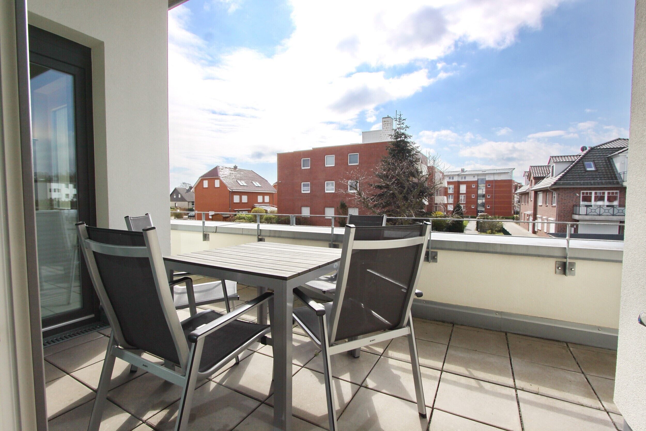 A balcony with a table and chairs, overlooking a residential area with red brick buildings.