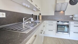 A modern kitchen with a stainless steel sink, built-in oven, and white cabinetry.