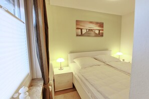 Une chambre à coucher avec un lit, deux tables de chevet, une commode, une lampe et un tableau au mur.