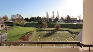 Vista da un balcone su un parcheggio con un'area verde e alberi.