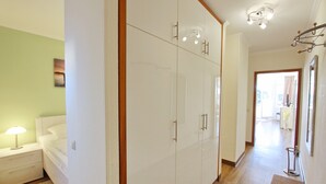 Una camera d'albergo con un letto, un comodino, un armadio e un corridoio che porta al bagno.