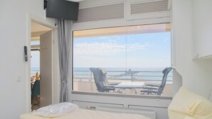 A hotel room with a large window overlooking a beach and a dining area. - Grömitz-center I App. 657 Inkl. Wlan (Grömitz)