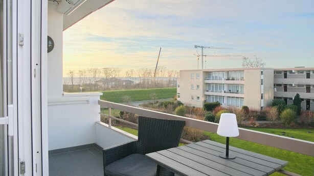 A balcony with a table and chair, overlooking a construction site and residential buildings. - Brookgang 47d Doppelhaushälfte Inkl. Wlan (Grömitz)