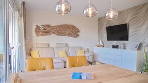 A modern living room with a sofa, yellow cushions, a wooden dining table, and pendant lights. - Brookgang 47d Doppelhaushälfte Inkl. Wlan (Grömitz)