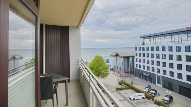 Ein Balkon mit Meerblick, ein Parkplatz und ein modernes Gebäude mit blauer Fassade.