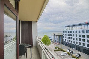 A balcony with a view of the sea, a parking area, and a modern building with a blue facade. - Grömitz-center I App. 648 (Grömitz)