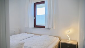 Ein Schlafzimmer mit einem Bett, einem Nachttisch, einer Lampe und einem Fenster mit Vorhängen.