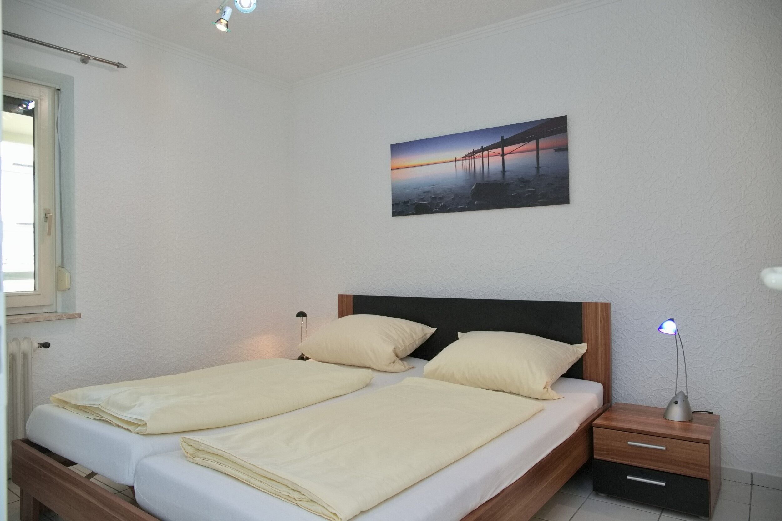 A double bed with two pillows, a nightstand with a lamp, and a framed picture on the wall.