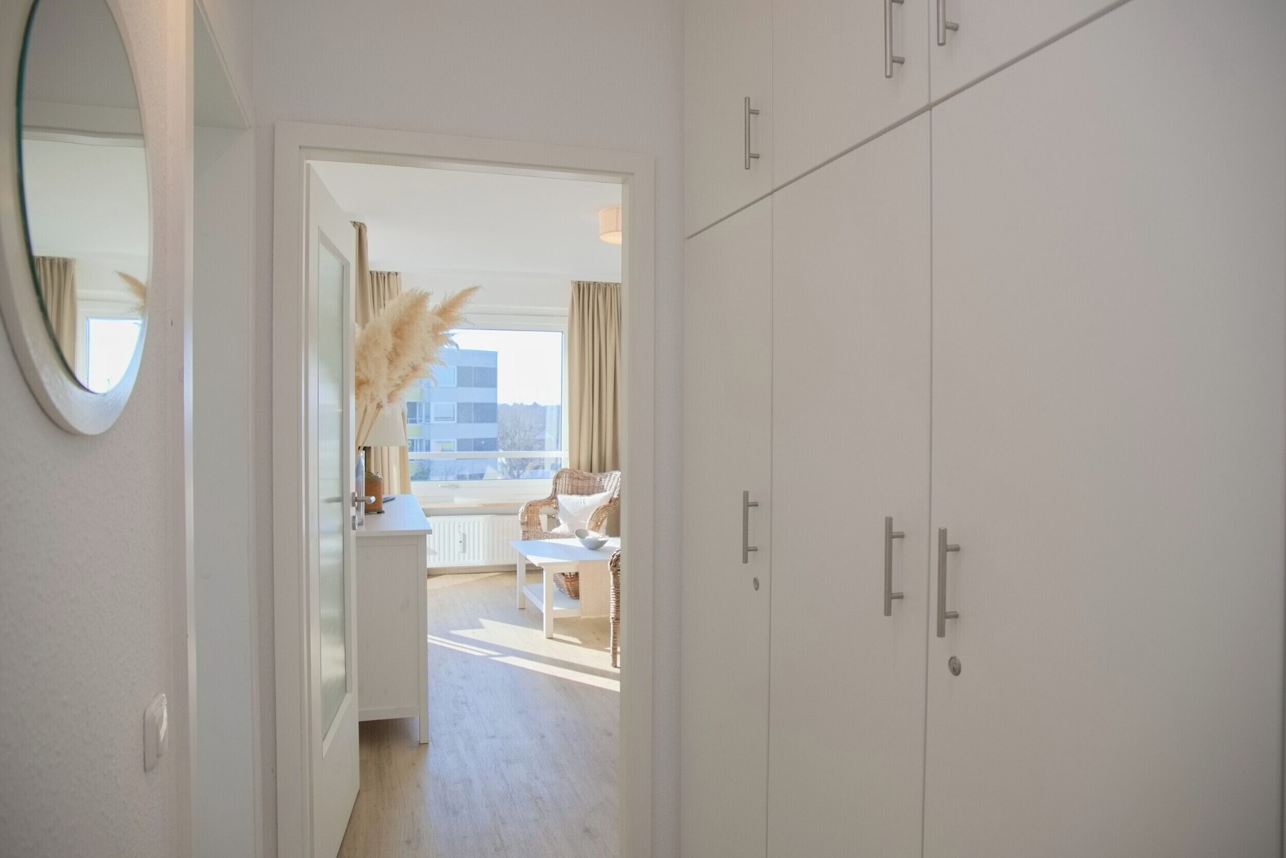 A hallway leading to a balcony with a view, white wardrobe, and a mirror.