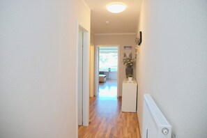 A hallway with wooden flooring, a radiator, and a door leading to a room with a window.