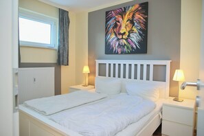 Una habitación de hotel con cama, dos lámparas de noche, un radiador y una ventana con cortinas.