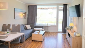 A modern living room with a sofa, a dining table, and a TV mounted on the wall. - Fürstenhof App. 108 Inkl. Wlan (Grömitz)