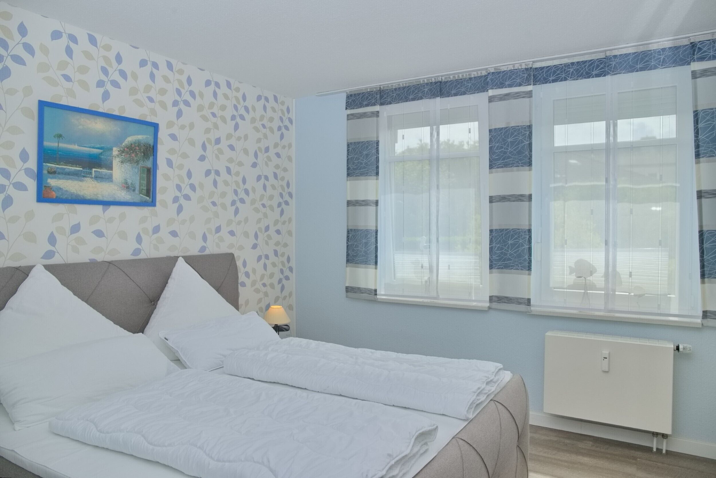 A bedroom with a bed, a nightstand, a window with curtains, and a wall with a leaf pattern.