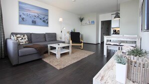 Un salon moderne avec un canapé gris, une chaise en bois, une table basse et une table à manger avec des chaises. Un tableau est accroché au mur et une plante est posée sur la table à manger.