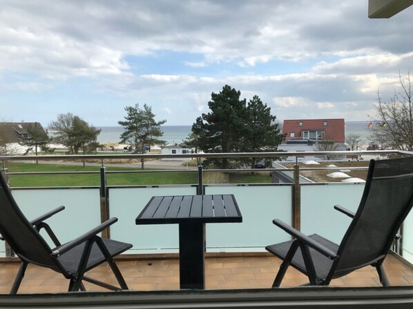 Un balcon avec deux chaises et une table, donnant sur un espace verdoyant et un immeuble situé de l’autre côté de la rue.