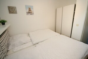 Un lit bien fait, avec une literie blanche, une décoration en forme de cœur accrochée au mur et un tableau représentant des pierres.