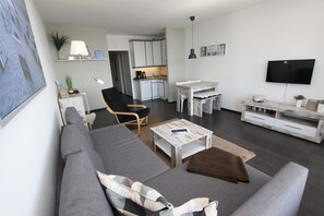 Un salon moderne avec un canapé gris, une table basse et un téléviseur. Il y a également un coin cuisine avec des placards et une table à manger.