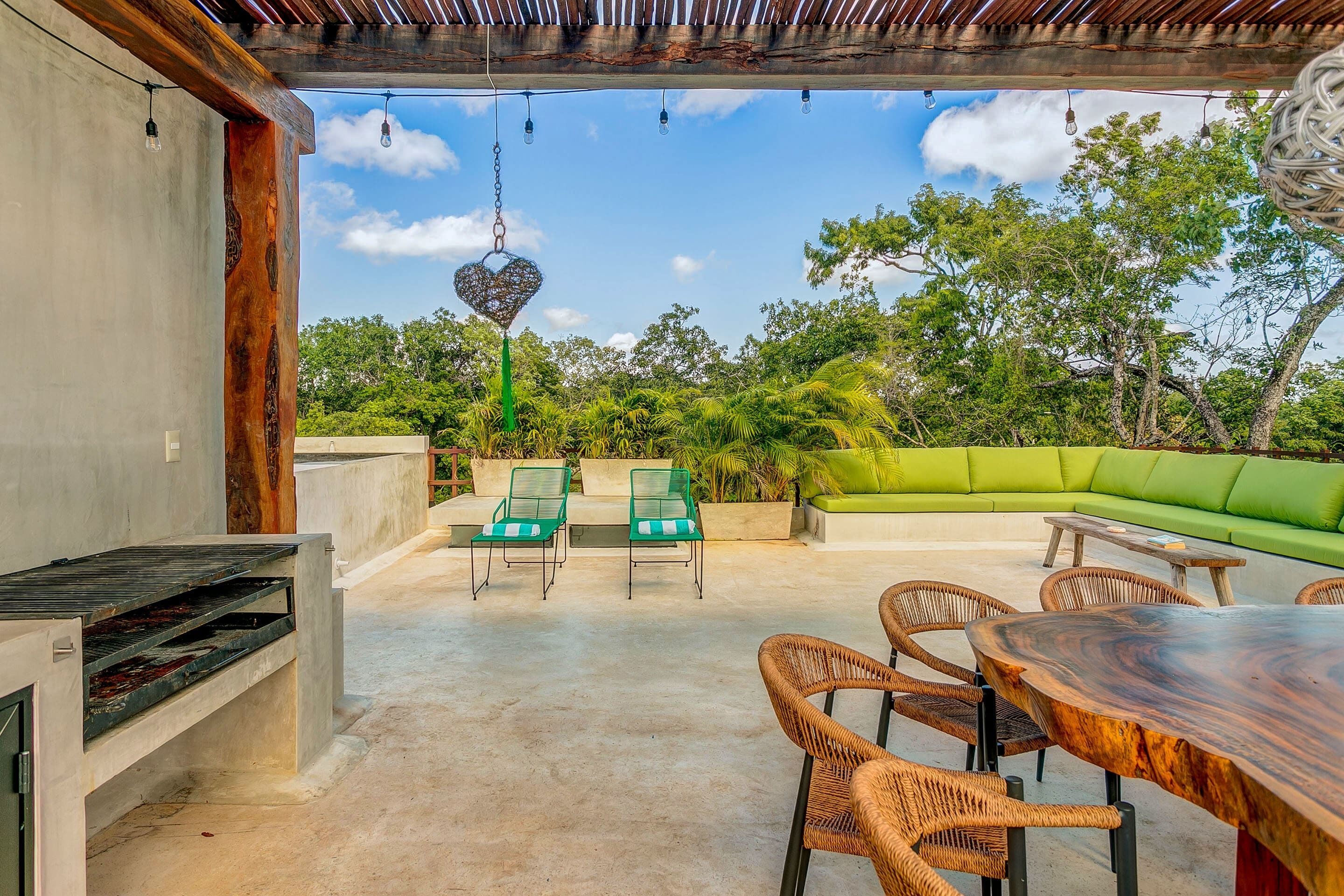 An outdoor patio with a wooden table and chairs, a green sofa, and a hanging heart-shaped decoration.