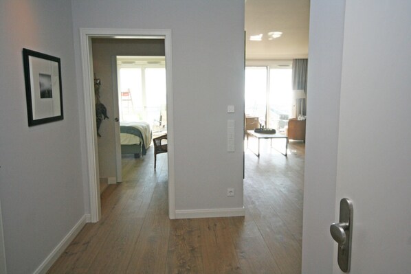 A hallway with a wooden floor, a framed picture on the wall, and a door leading to a room with a bed and a chair. - Seeblick Waterfront 2 Inkl. Wlan (Grömitz)