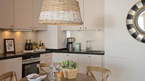 Uma cozinha moderna com armários brancos, bancada preta, luminária trançada e máquina de café.