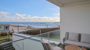 A balcony with a view of the beach and pier, a sofa, and a table.