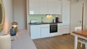A compact kitchen with white cabinets, a black oven, and a wooden dining table.
