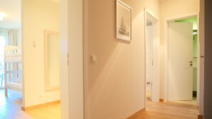 A hallway with a wooden floor, white walls, and a framed picture. There is a door leading to another room.