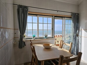 A dining area with a view of the ocean, a wooden table, and two chairs. - Bela Vista Apartment by Acasadascasas (Mafra)