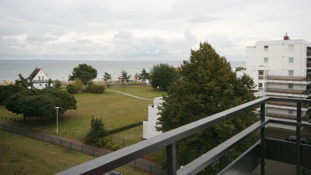 A view from a balcony overlooking a grassy area with trees and a body of water in the background. - Prinzenhof App. 26 (Grömitz)