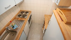 A compact kitchen with white cabinets, a stainless steel sink, a stove, and a wooden countertop. - Prinzenhof App. 26 (Grömitz)