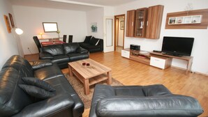 A living room with a sectional sofa, a coffee table, a TV stand, and wooden cabinets. - Prinzenhof App. 26 (Grömitz)