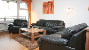 A living room with a black leather sofa, a wooden coffee table, and a floor lamp. - Prinzenhof App. 26 (Grömitz)