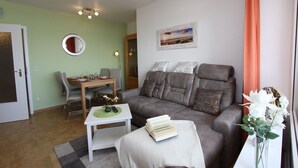 Un salon avec un canapé gris, une table basse blanche, une table à manger avec des chaises, un miroir et un tableau accroché au mur.