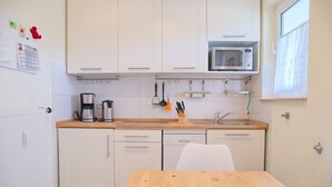 Een compacte keuken met witte kasten, een magnetron, een koffiezetapparaat en een houten tafel.