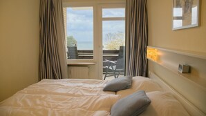 Een hotelkamer met een bed, uitzicht op zee door een deur en een tafel met stoelen buiten.