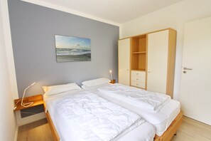 Une chambre avec deux lits, une armoire en bois, une table de chevet et un tableau au mur.